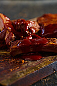 High angle of appetizing grilled pork ribs with barbecue served on wooden board in kitchen against blurred background