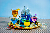 Verschiedene Cocktails, darunter eine blaue Margarita Long Island Eistee Wein Daiquiri in attraktiven Gläsern und Gläsern auf einem Teller auf gestreiftem Tuch vor blauem Hintergrund