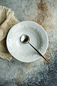 Top view of autumnal table setting with white ceramic bowl and spoon on napkin against gray surface