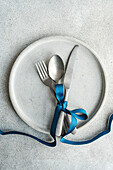 Top view of minimalist yet stylish Easter table setting, with cutlery tied together with blue ribbon on concrete plate, placed on gray table