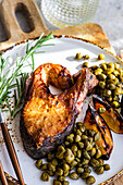 Close-up of a barbecued salmon steak seasoned with spices served with roasted lemon slices and capers garnished with rosemary