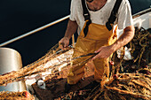 Von oben abgeschnittener unkenntlicher männlicher Fischer in Uniform, der mit einem Netz auf Fischfang geht, während er auf einem Schoner in Soller nahe der Baleareninsel Mallorca arbeitet
