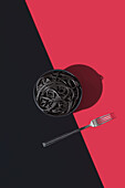 Top view of black spaghetti in a bowl placed on black and red background near fork