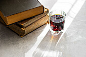 Kirschlikör in einem klaren Glas neben einem Stapel alter Bücher auf einer sonnenbeschienenen Fläche