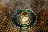 A creatively plated fusion dish from a Michelin-starred restaurant in Zermatt, Switzerland, combining local and seasonal ingredients with smoke for a dramatic effect.