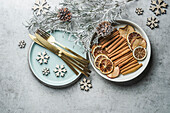 Christmas table setting with golden cutlery, pale blue plate, cinnamon sticks, dried orange natural dried apples and oranges and winter branches on grey table. Top view.