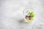 Top view transparent glass of refreshing cold drink with lime and cherry and mint leaves on gray surface in summer day against blurred background