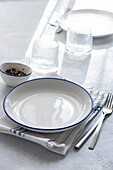 A stylish dining setup featuring a white plate with blue rim, cutlery, and glassware arranged on a textured tablecloth.