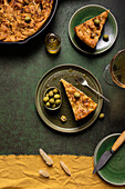 Top view of slice baked Italian focaccia bread with green olives in plate on dining table with drink on green background