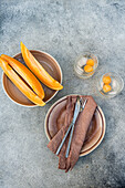 Top view of sliced organic fresh orange musk melon fruit and melon spheres in transparent glasses with ice cubes while served on table with napkin fork and knife in daylight