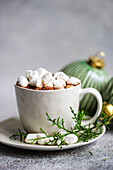 Köstlicher Kakao mit Marshmallow auf einem Teller mit Tannenzweigen in der Nähe von Weihnachtskugeln