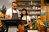 Positive young multiracial coworkers in aprons positive and using monitor to enter information while standing at counter together during work