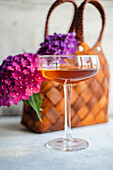Glass with fresh drink placed on table near bouquet of purple hydrangeas inside brown bag basket