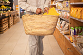 Cropped unrecognizable male customer in casual clothes standing near shelves with goods while shopping with bag in grocery shop
