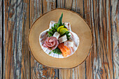 Traditionelles japanisches Sashimi-Gericht mit verschiedenen rohen Fischen in einer Muschelschale auf Holzuntergrund von oben