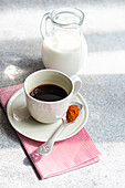 High angle of cup of spicy espresso near spoon with red paprika on gray table near bottle of milk in daylight