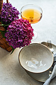 Top view of purple hydrangea placed on white table near ceramic plates and glass with drink