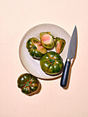Grüne Tomaten in hellem Sonnenlicht flach über Teller mit Messer mit Kopie Raum auf beige Hintergrund legen