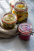 Three jars with assorted fermented vegetables, including cabbage with beetroot, spicy peppers, and white cucumbers, presented in a sunny kitchen setting.