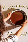 Overhead view of an anonymous person taking a bowl filled with chocolate placed on table with floral tablecloth