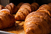 Nahaufnahme von frisch gebackenen, köstlichen, knusprigen Croissants, die auf einem Metalltablett im Ofen in der Bäckereiküche liegen