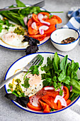 A ketogenic diet-friendly meal with poached eggs, fresh vegetables, and leafy greens served on a white and blue rimmed plate.