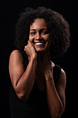Positive Hispanic young female with curly hair touching face and looking at camera while standing on black background