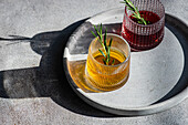 From above of artisanal cocktails with vodka cherry, and apple juice in textured glasses adorned with rosemary on a concrete surface with shadows