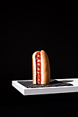 Appetitliches Brötchen mit Wurst und Ketchup auf weißem Holzbrett vor schwarzem Hintergrund im Studio