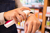 Crop unrecognizable male in casual clothes indoors in shop and applying body cream to back of hand while standing against blurred camera