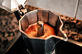 Nahaufnahme von blubberndem Kaffee in einer offenen Espressomaschine, die das reiche Aroma und die Konsistenz von frisch gebrühtem italienischen Kaffee in einer gemütlichen Umgebung einfängt