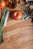 Reife Tomaten, Spargel und Lauch mit Olivenöl und Oliven auf einem rustikalen Holzschneidebrett, ideal für kulinarische Hintergründe