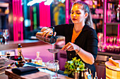 Beautiful confident young female barkeeper standing while straining drink from shaker at bar counter while working in nightclub