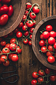 Top view of bunch with ripe red cherry tomatoes placed on wooden table in bowls