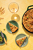 Top view of flat leavened oven-baked Italian focaccia bread in pan served with fresh green olives and honey in bowls on yellow background surface