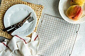 Draufsicht auf saisonale Pfirsiche, die auf einem Teller mit Gabel und Messer serviert werden, der auf dem Tisch neben einer Serviette und einem Ofengestell steht