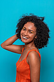 Side view of smiling African American female model in casual clothes with dark curly hair looking at camera against blue background