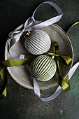 Top view of balls decorated with colorful satin ribbon as symbol of Christmas time placed ceramic bowl on gray surface