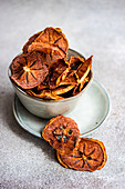 High angle of slices of dried apples served in ceramic bowl on plate against blurred gray background