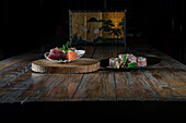 Appetizing sashimi of raw tuna and salmon in white plate on wood slice while sushi rolls made with rice avocado fish in black plate and served on table against dark background