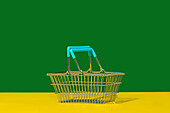 Empty metal basket with blue handles placed on yellow table against green wall