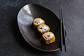 Von oben Reihe von leckeren gebratenen Sushi-Rollen mit gekochtem Reis und Lachs mit Avocado-Scheiben auf schwarzem Keramikteller auf Tisch