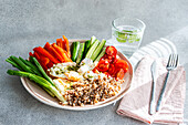 A fresh and healthy breakfast dish showcasing a variety of raw vegetables, creamy feta, wholesome buckwheat, and fried eggs, all drizzled with pesto sauce.