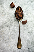 Top view of pieces of different kinds of chocolate placed on crop spoon and on gray blurred table