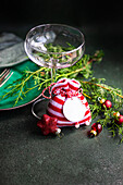 Glas mit kleiner rot-weißer Tasche neben Tannenzweigen auf dunkler Oberfläche in der Weihnachtszeit