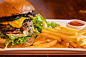 Hausgemachter Cheeseburger mit Käse und Gemüse, serviert mit Pommes frites und Salat