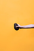 Crop anonymous kid with hand demonstrating ripe dark avocado against yellow background in studio