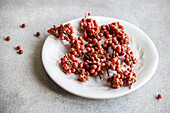 Focus of scattered organic buffaloberries on a white ceramic plate with a few berries fallen on the grey surface in soft daylight