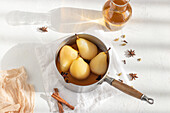 From above saucepan with delicious poached pears in white wine at table near star anise and jar with juice