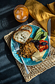 Top view of five ingredients lunch set consists of homemade goat cheese, fresh cucumber and tomato with leaves of basil herb, in addition to fried rice with meat with slices of healthy sour dough bread served with glass of carrot-apple juice against gray background